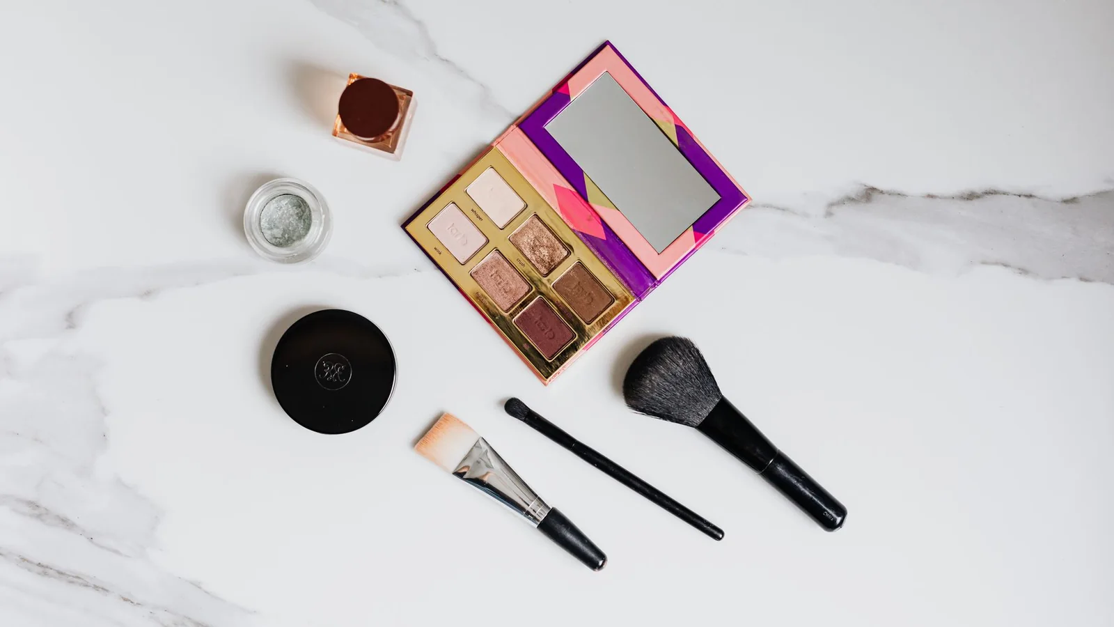 Pequeños productos de maquillaje organizados junto a una bolsa de viaje